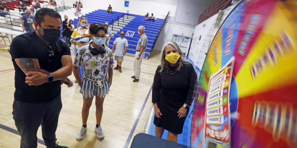 Vax 2 the Max: Federico Garcia and his daughter, Kassandra Garcia, 14, wait to see how many scratch-off tickets they will win as Gov. Michelle Lujan Grisham spins the prize wheel for them at a vaccination event last month at Desert Sage Academy. Luis Sánchez Saturno/New Mexican file photo