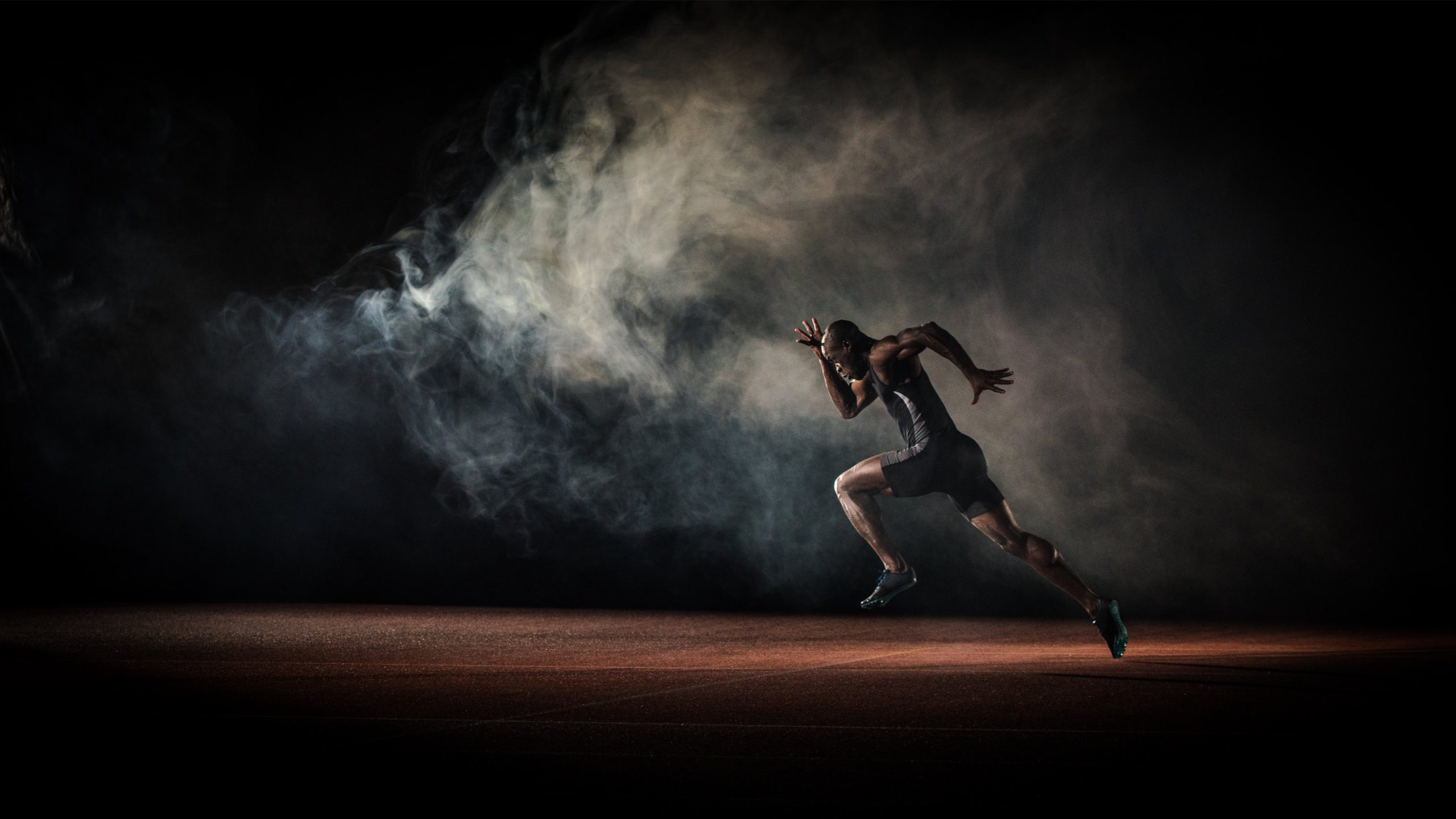 A sprinter drives out of the start through smoke on a red track.